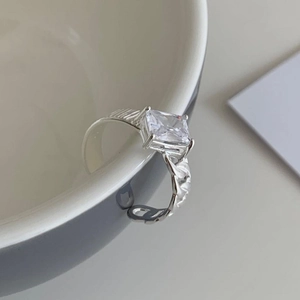 Minimalist 925 sterling silver ring with square zircon stone hanging on a white ceramic cup