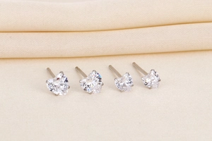 Macro shot of silver heart stud earrings with sparkling cubic zirconia on beige fabric