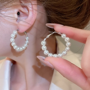 Detail shot of a model wearing elegant white pearl hoop earrings with silver-tone metal