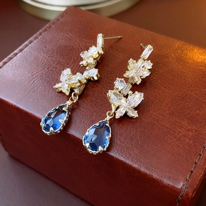 Detail of gold butterfly earrings with zircon inlay and blue water drop gemstone pendants