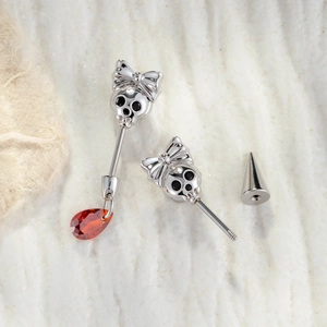 Bow skull belly button ring with red teardrop gem on a textured white surface
