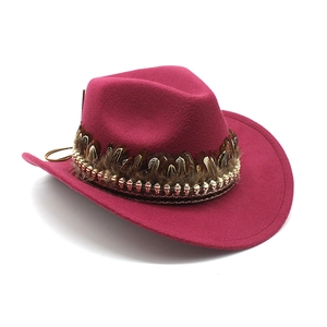 Detail of magenta wool cowboy hat featuring brown feather band and gold skull accents