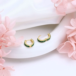 Close-up of golden hoop earrings with emerald green zircons on elegant white silk background