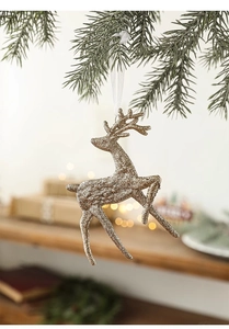 Detail of glittery gold reindeer ornament hanging on a green pine branch with warm lights