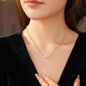 Close-up of a gold tennis necklace with pink and white round zircon stones on a model