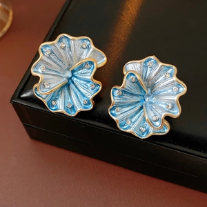 Close-up of blue enamel flower earrings with gold edges and rhinestones on black leather