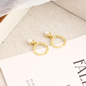 Macro shot of gold hoop earrings featuring polished white pearl pendants on beige fabric