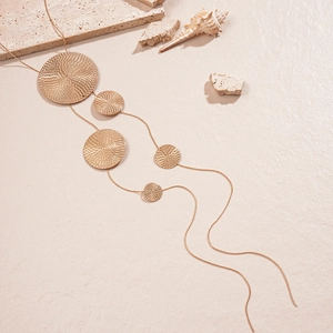 Long gold tassel sweater necklace with circular engraved pendants and minimalist metal texture