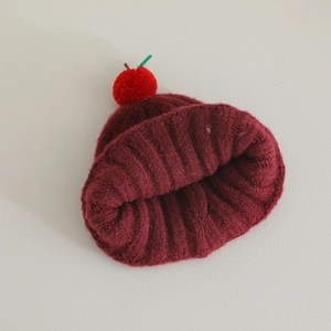 Detail of burgundy ribbed knit hat with cute cherry pom-pom and green stem decoration