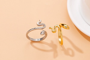 Detail van slangvormige ringen in goud en zilver op een warme beige achtergrond met schaduw
