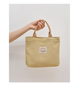 Detail of bear embroidery patch and sturdy handle on mustard yellow canvas tote bag