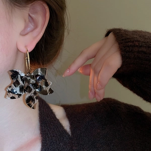 Detailed view of oversized leopard print flower earrings on a model with metal hoops