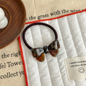 Detailed view of handmade acetate tortoiseshell bow hair tie on a decorative tray