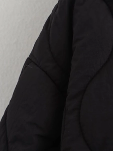 Detail view of black quilted jacket featuring curved stitching and premium woven fabric