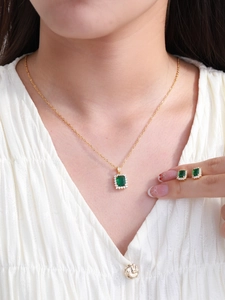 Close-up of elegant gold jewelry set with rectangular emerald stones on a model