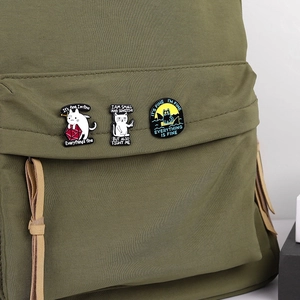 Trois pin's chat noir en émail avec dés et texte sur une bretelle de sac à dos