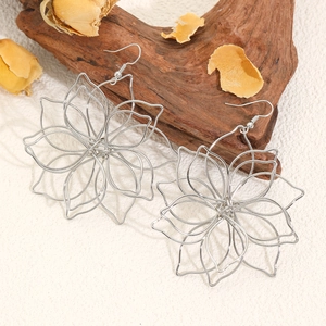 Detailed close-up of hollow silver flower earrings on wooden block with dried petals