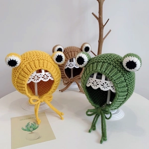 Three knitted baby frog hats in yellow, brown and green with earflaps and big eyes