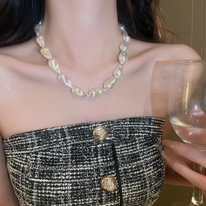 Baroque pearl necklace on a model in a black and white tweed top holding a glass