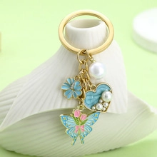 Detail of gold keychain with pearl, blue floral heart and butterfly charms on ceramic stand