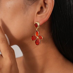 Macro shot of red enamel flower earrings with gold trim on model for a vintage aesthetic