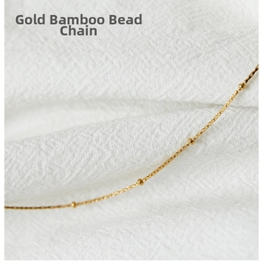 Detail of gold bamboo style chain with small round beads on white texture background