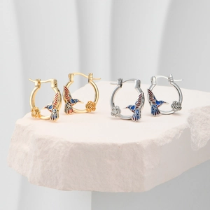 Artistic display of gold and silver hummingbird hoop earrings with rose and enamel details