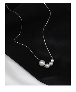 Detailed view of four gradient white pearls on a silver chain necklace over black fabric