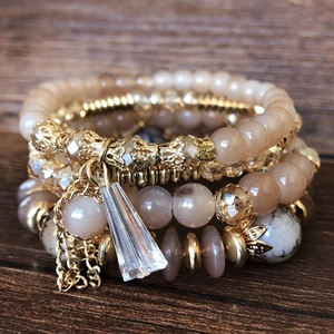 Close-up of bohemian stacked bracelets with gold accents and marble beads on wood