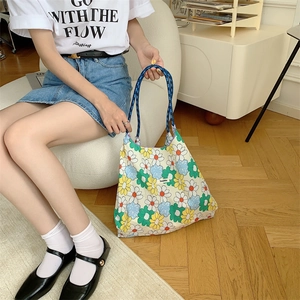 Detail of floral canvas tote bag with blue woven handles held in a casual lifestyle setting