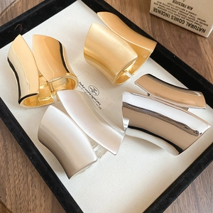 Close-up of wide irregular metal bangles in glossy and matte gold and silver finishes