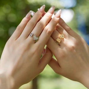 Macro shot of gold and silver letter B heart rings with zircon stones on fingers