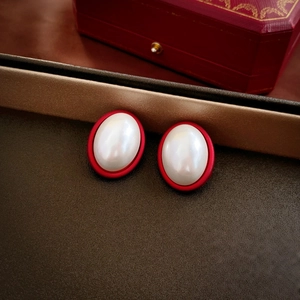 Macro detail of red and pearl oval vintage earrings on a dark textured background