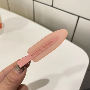 Pink matte jelly hair clip with seamless metal base held by hand on white tile background