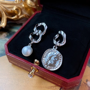 Detailed close-up of asymmetric pearl and silver coin earrings in a red velvet jewelry box