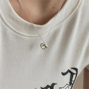 Close-up of minimalist silver hollow heart knot necklace worn on a model wearing white
