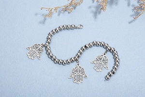 Silver Hamsa beaded bracelet with three filigree hand charms on light blue background
