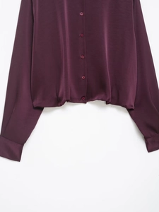 Detail of burgundy satin shirt featuring button-down front and elastic hemline texture