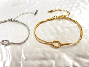Detail of gold and silver herringbone snake bracelets with center knot and K18 tag