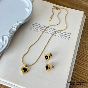 Minimalist gold snake chain jewelry set with black heart pendants on an open book