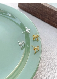 Detail view of gold and silver bow stud earrings on a ceramic dish with soft lighting