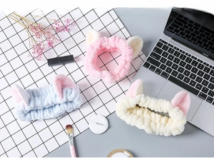 Three plush cat ear headbands in pink, blue, and white, displayed with beauty accessories