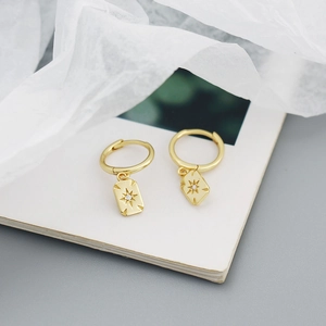 Detail view of gold rectangle starburst earrings with zircon inlay on book pages