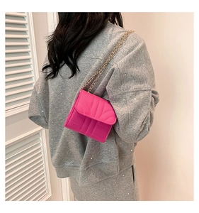 Close-up of rose red quilted crossbody bag with elegant gold chain strap on a model