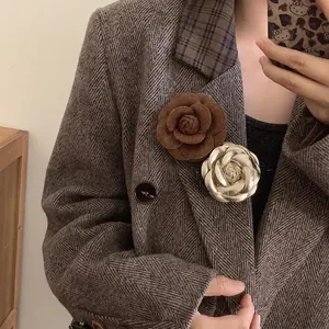 Elegant leather and gold camellia flower brooches pinned on a brown tweed blazer