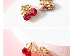 Macro view of cherry-shaped charms with red rhinestones and gold plating details