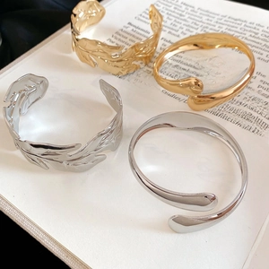 Detailed view of four metal leaf and teardrop open bangles on an open book