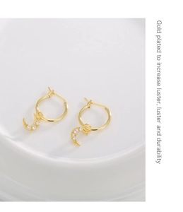 Close-up of gold plated moon earrings with clear cubic zirconia on white ceramic tray