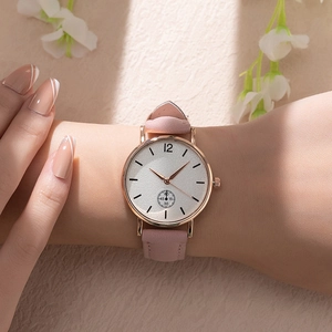 Close-up of a pink quartz watch with rose gold case and suede strap worn on a wrist