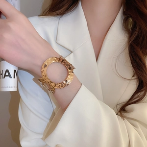 Detail of wide hammered gold cuff bracelet with irregular texture on a model's wrist